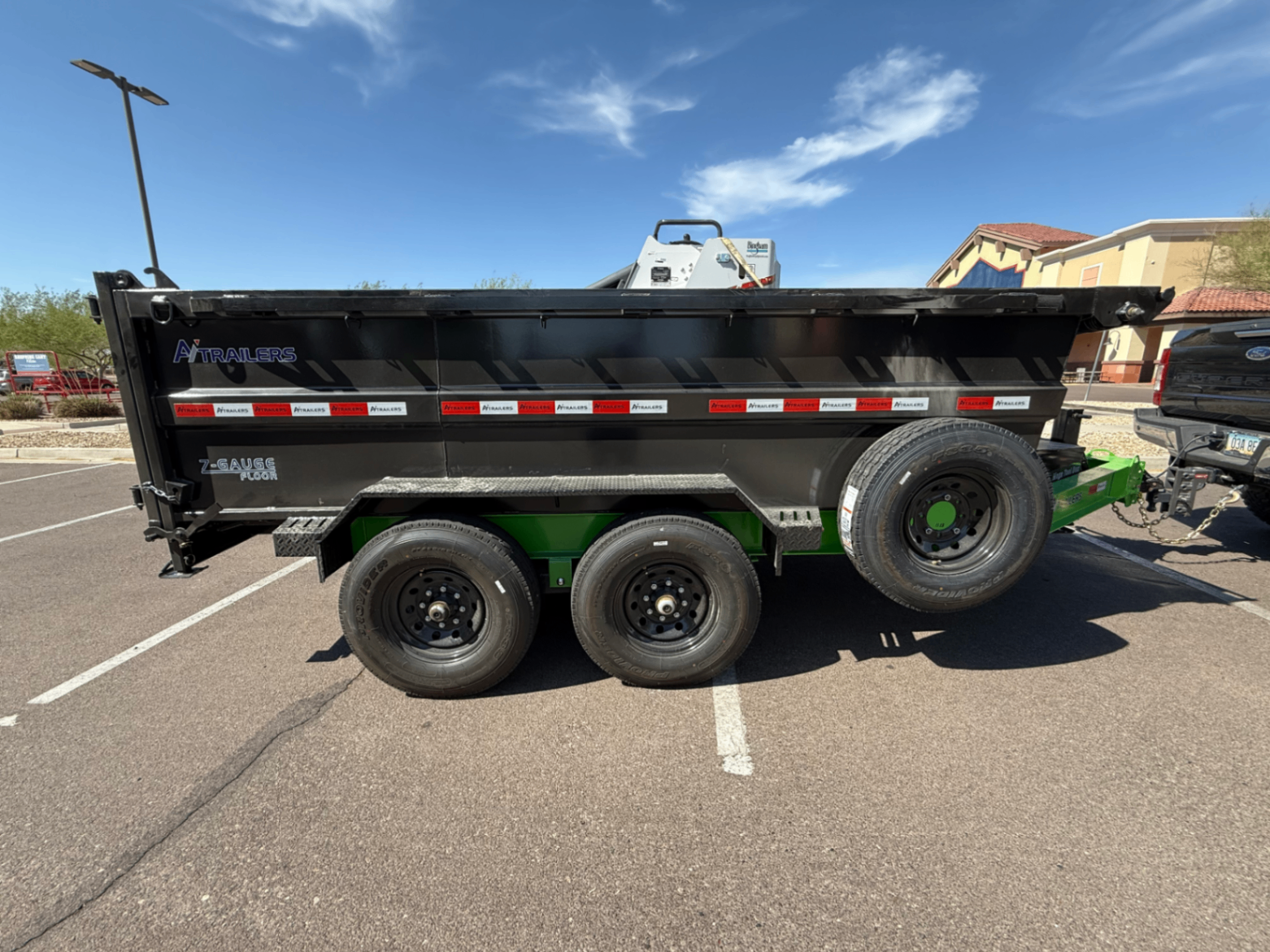 Black triple-axle dump trailer with green accents, side view.