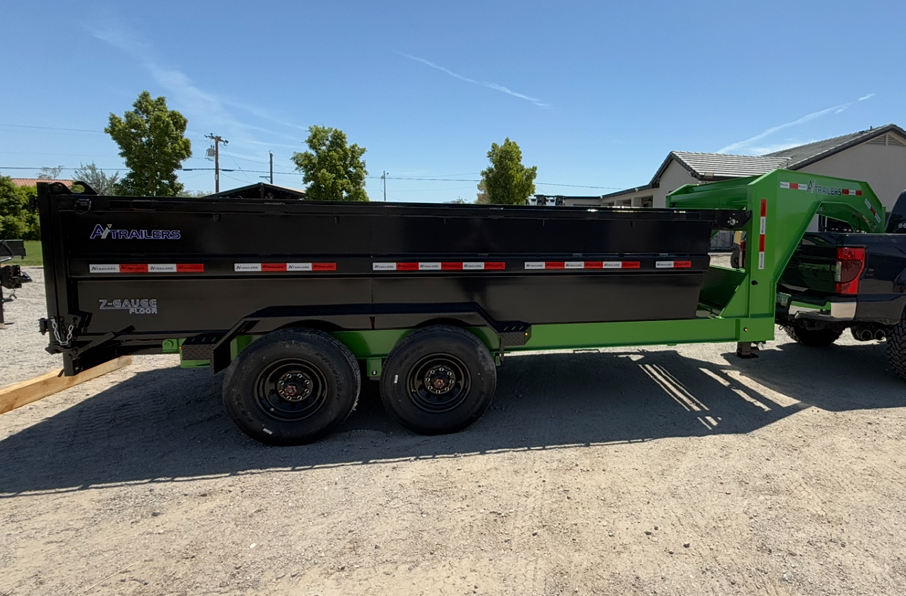 Black gooseneck dump trailer with a green chassis parked in a lot.