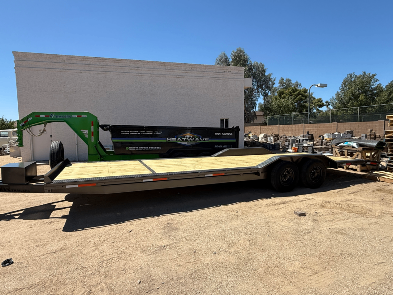 28 foot gray car hauler trailer with new wood deck, drive-over fenders and rear ramps, parked in a gravel lot.